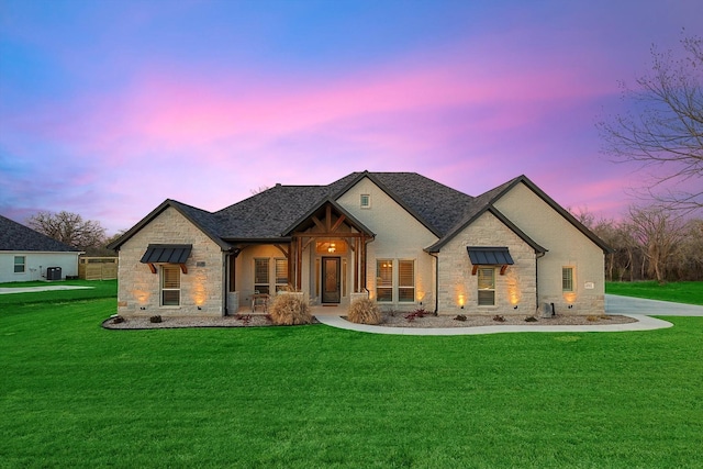 back of property at dusk featuring a lawn, a shingled roof, and stone siding