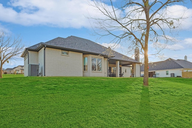 rear view of house featuring a shingled roof, a yard, and brick siding