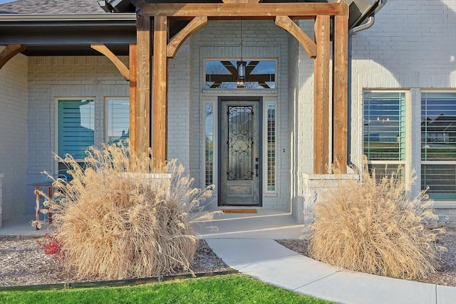 entrance to property featuring roof with shingles and brick siding