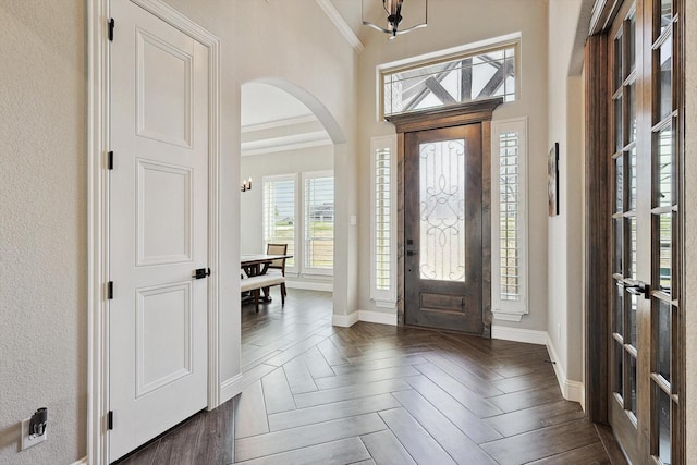 entrance foyer featuring crown molding, arched walkways, and baseboards