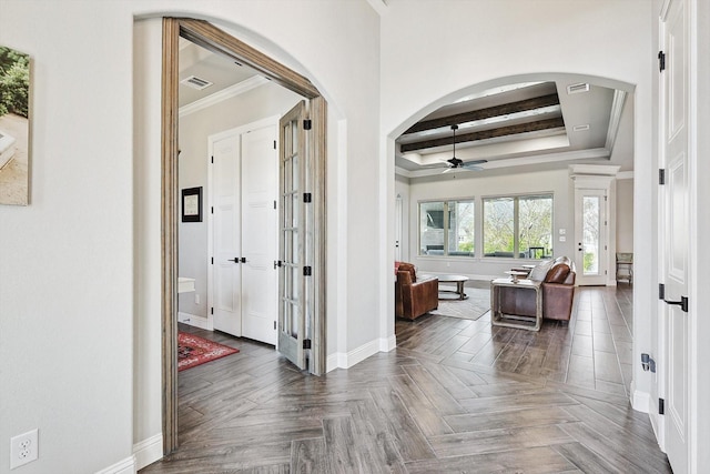 corridor featuring baseboards, arched walkways, a tray ceiling, and visible vents
