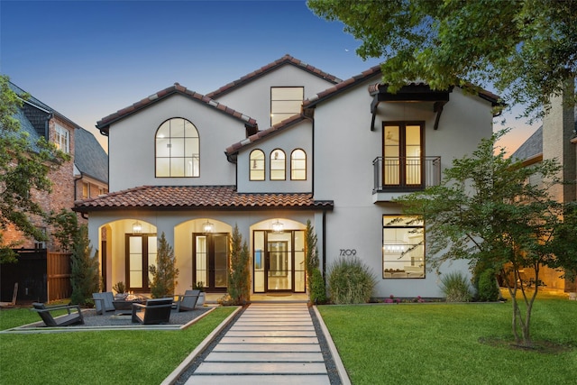 back of house with a lawn, stucco siding, a balcony, and a tiled roof
