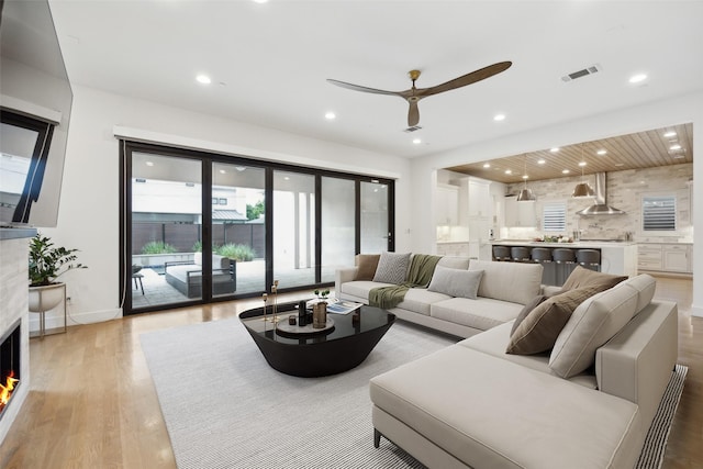 living room with visible vents, ceiling fan, a warm lit fireplace, recessed lighting, and light wood-type flooring