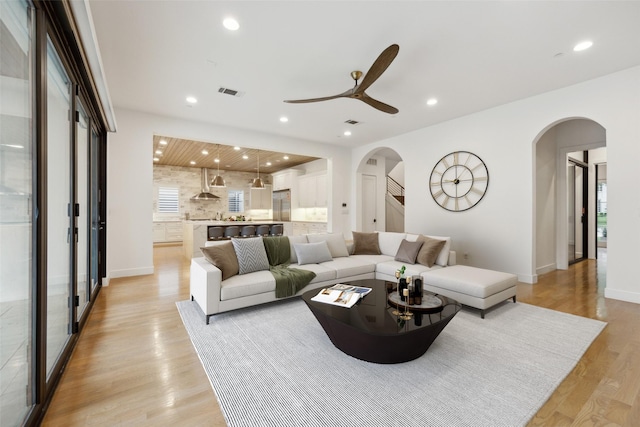 living area featuring visible vents, light wood-style floors, ceiling fan, recessed lighting, and arched walkways
