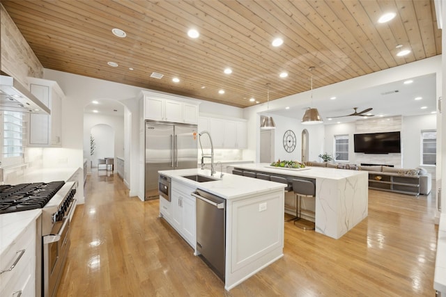 kitchen with high quality appliances, a sink, a kitchen island with sink, arched walkways, and open floor plan