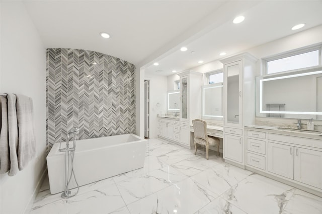 full bathroom with two vanities, a sink, an accent wall, a soaking tub, and recessed lighting