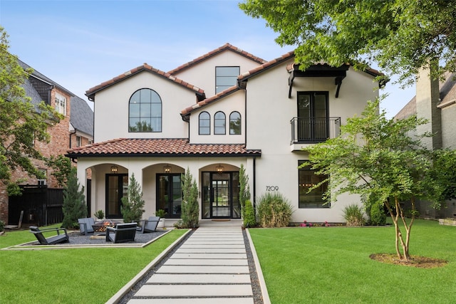 back of property featuring a yard, a tiled roof, a balcony, and stucco siding