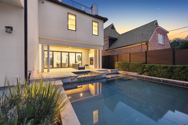 back of property at dusk featuring a patio, a pool with connected hot tub, fence, and stucco siding