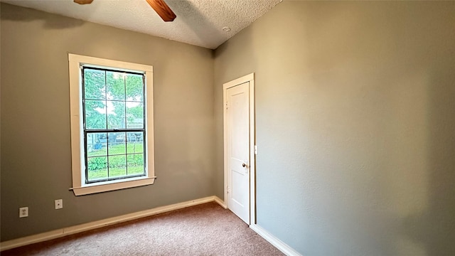 spare room featuring dark colored carpet, a textured ceiling, ceiling fan, and baseboards