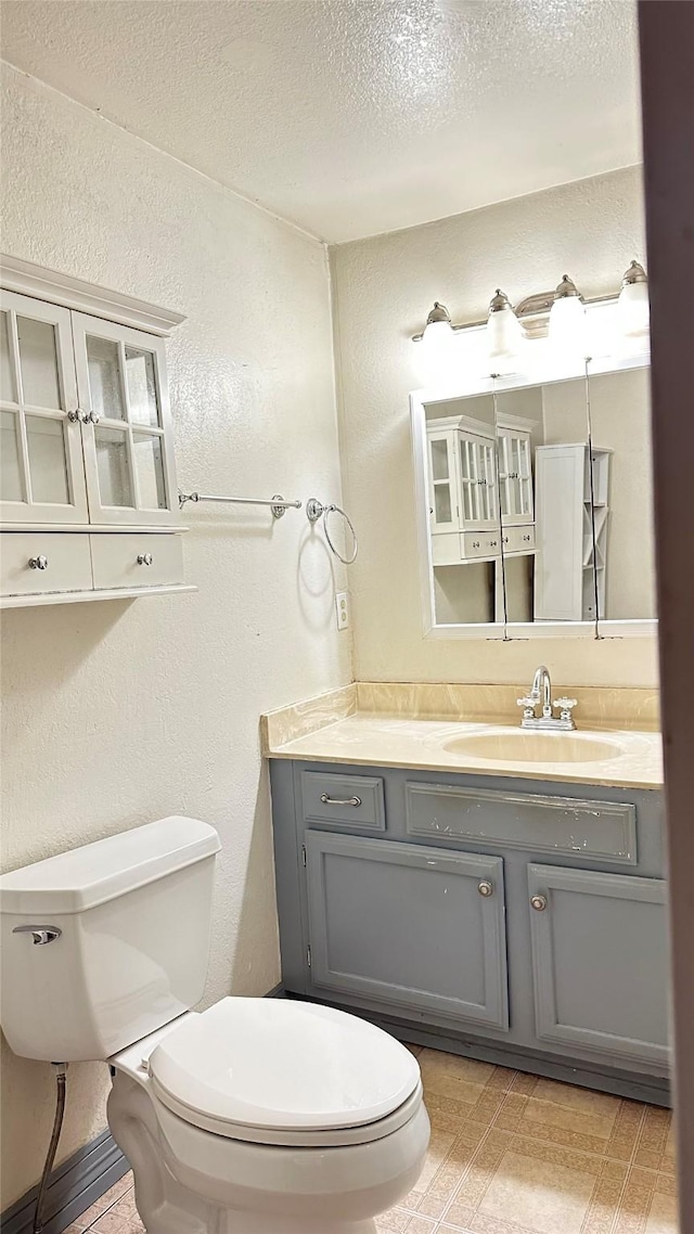bathroom with vanity, toilet, a textured wall, and a textured ceiling
