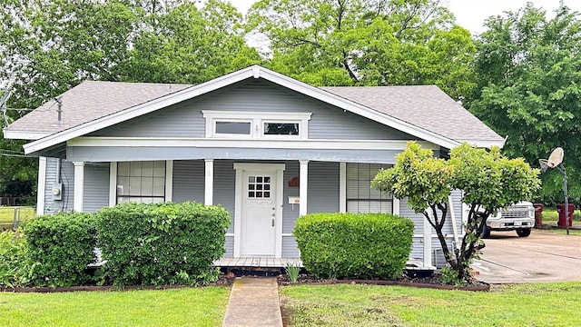 bungalow featuring covered porch, roof with shingles, and a front lawn