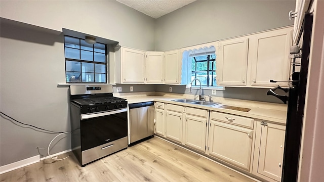 kitchen featuring appliances with stainless steel finishes, a sink, light countertops, a textured ceiling, and light wood-type flooring
