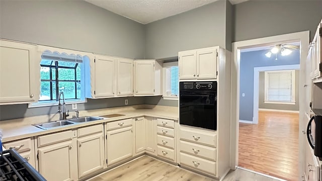 kitchen featuring oven, a sink, a textured ceiling, a ceiling fan, and light wood-type flooring