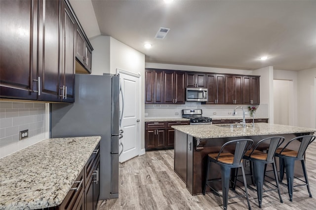 439 Tommie Lillian Ln, Celina, TX 75009 - kitchen featuring a breakfast bar area, light wood finished floors, a sink, tasteful backsplash, and appliances with stainless steel finishes