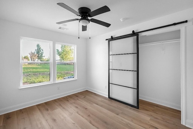 unfurnished bedroom with baseboards, visible vents, a barn door, and light wood-style floors
