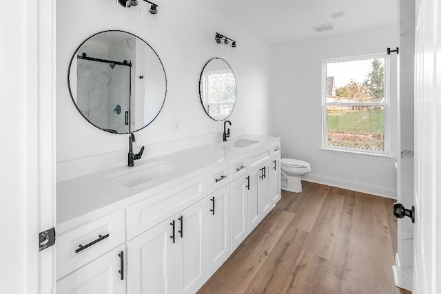 bathroom featuring a sink, a marble finish shower, toilet, and wood finished floors