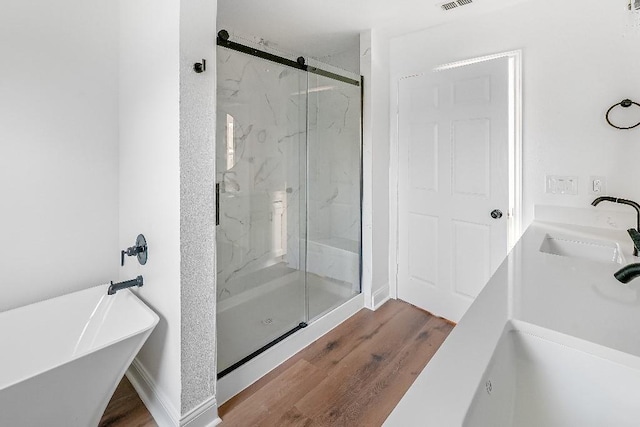 full bath with a freestanding bath, a marble finish shower, double sink, and wood finished floors