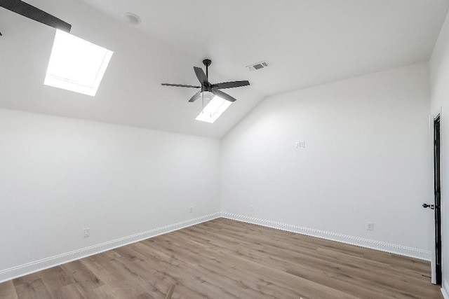 interior space featuring vaulted ceiling with skylight, a ceiling fan, visible vents, wood finished floors, and baseboards