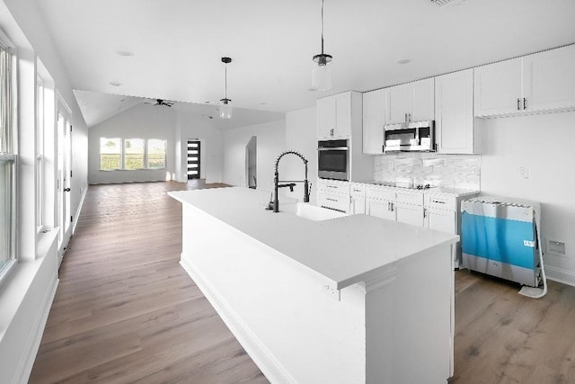 kitchen with white cabinets, a sink, light wood finished floors, backsplash, and stainless steel appliances