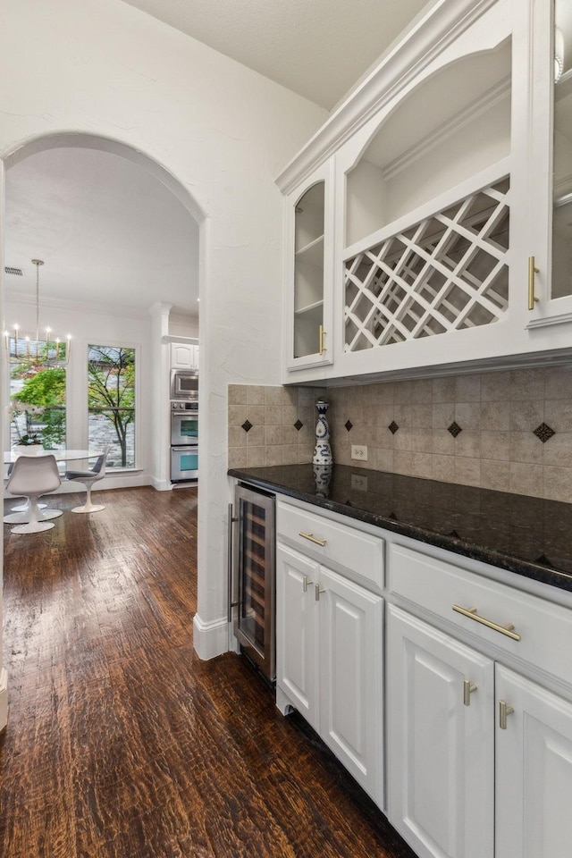 bar featuring decorative backsplash, wine cooler, a bar, arched walkways, and stainless steel appliances