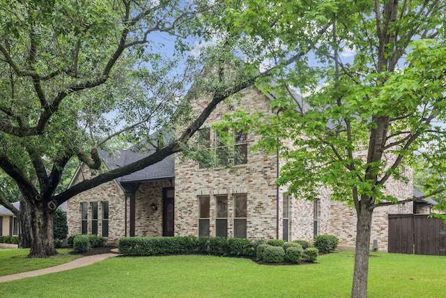view of front facade with brick siding, fence, and a front lawn
