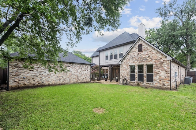 back of house featuring a chimney, brick siding, a shingled roof, central air condition unit, and a yard
