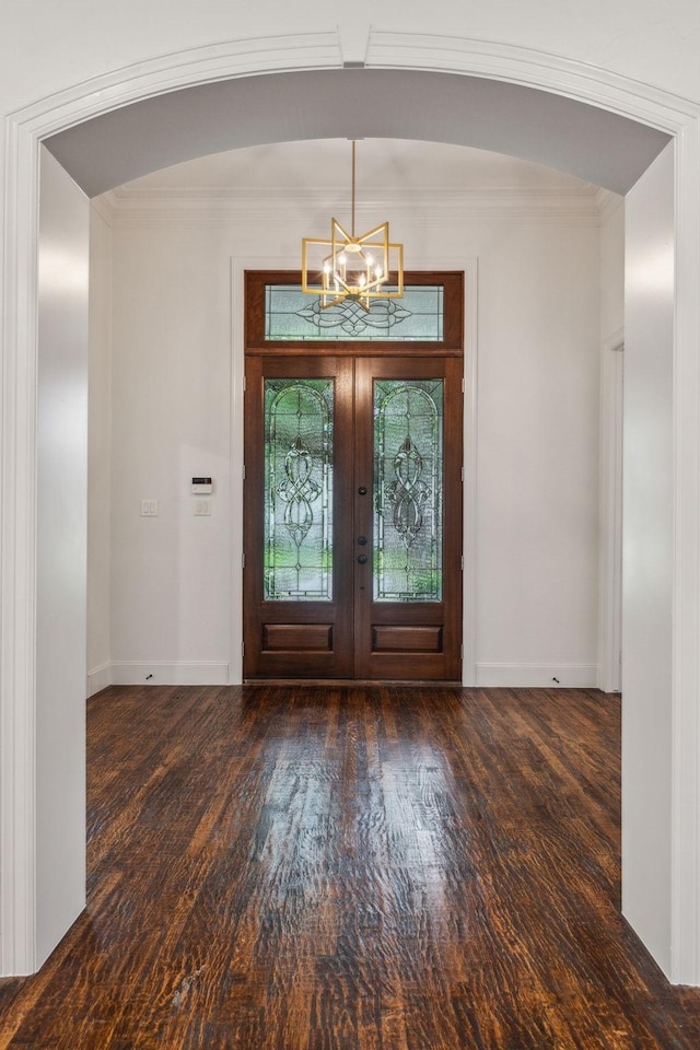 foyer with ornamental molding, wood finished floors, baseboards, arched walkways, and a notable chandelier