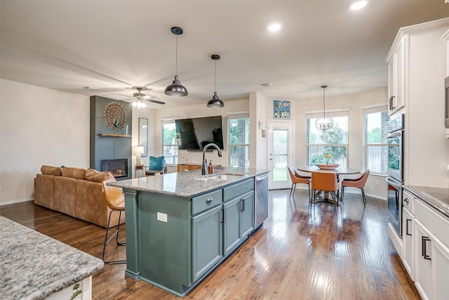kitchen with a sink, a fireplace, white cabinets, a ceiling fan, and appliances with stainless steel finishes