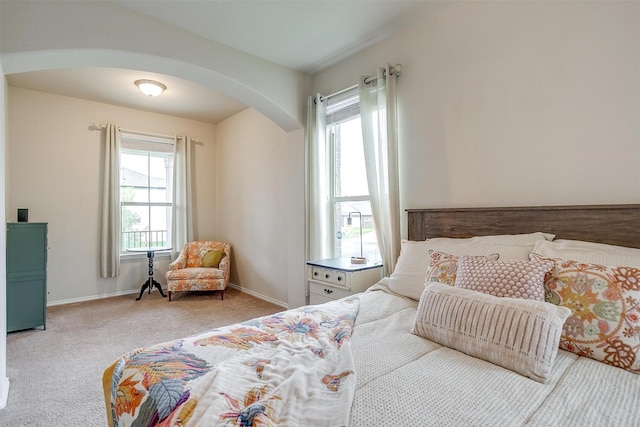 carpeted bedroom featuring arched walkways and baseboards