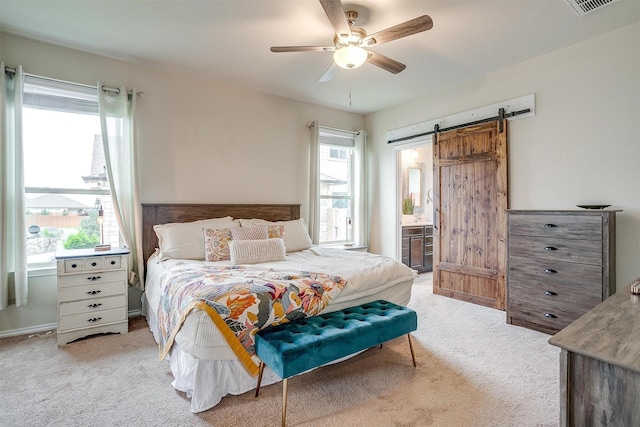 bedroom featuring ceiling fan, visible vents, light colored carpet, a barn door, and ensuite bath