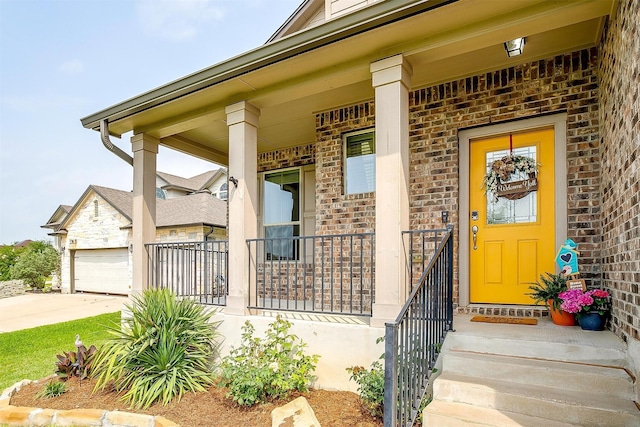 view of exterior entry with a garage, a porch, driveway, and brick siding