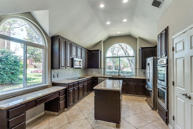 kitchen featuring light stone countertops, a center island, a sink, vaulted ceiling, and stainless steel appliances