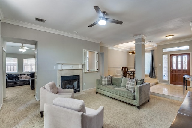 carpeted living area with a ceiling fan, visible vents, a tiled fireplace, and ornamental molding