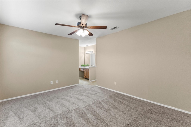 empty room featuring a ceiling fan, light colored carpet, visible vents, and baseboards