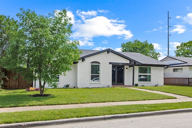 ranch-style home with fence, a shingled roof, brick siding, and a front yard