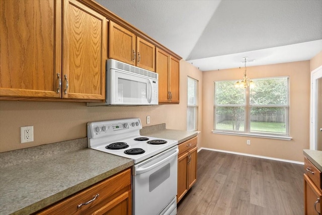 kitchen featuring white appliances, brown cabinetry, lofted ceiling, wood finished floors, and a chandelier
