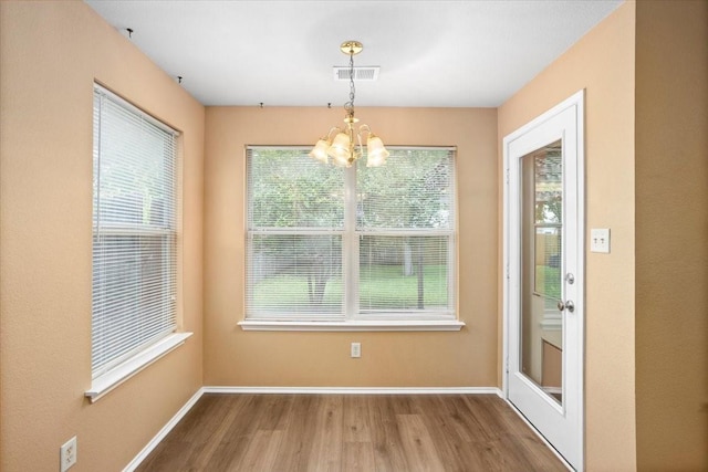 unfurnished dining area featuring wood finished floors, a chandelier, and baseboards