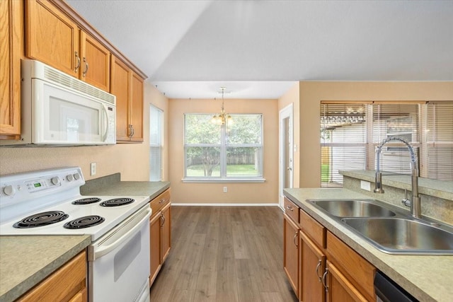 kitchen featuring white appliances, a sink, vaulted ceiling, brown cabinetry, and wood finished floors
