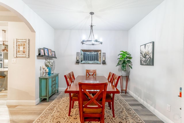 dining room with light wood-style floors, arched walkways, an inviting chandelier, and baseboards