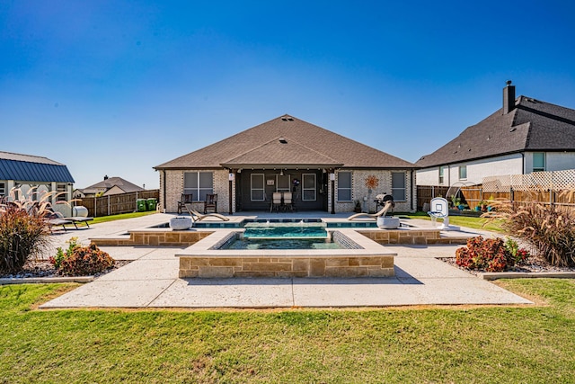 back of house with an in ground hot tub, a lawn, a patio area, brick siding, and fence