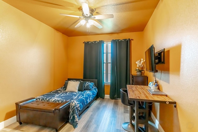 bedroom featuring baseboards, ceiling fan, a textured wall, and wood finished floors