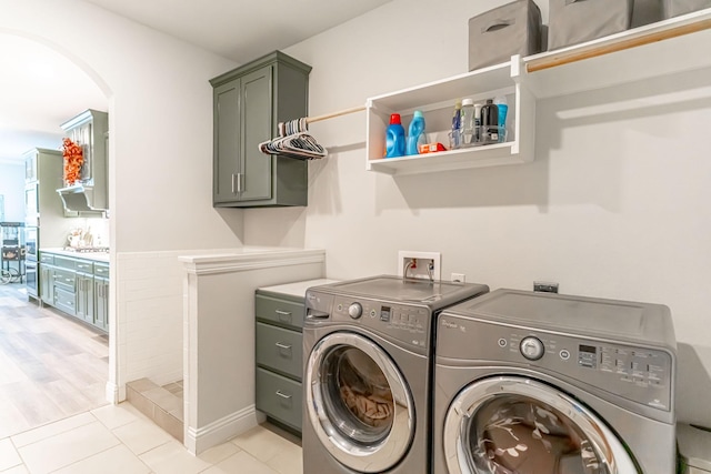clothes washing area featuring washing machine and clothes dryer, arched walkways, light tile patterned floors, and cabinet space