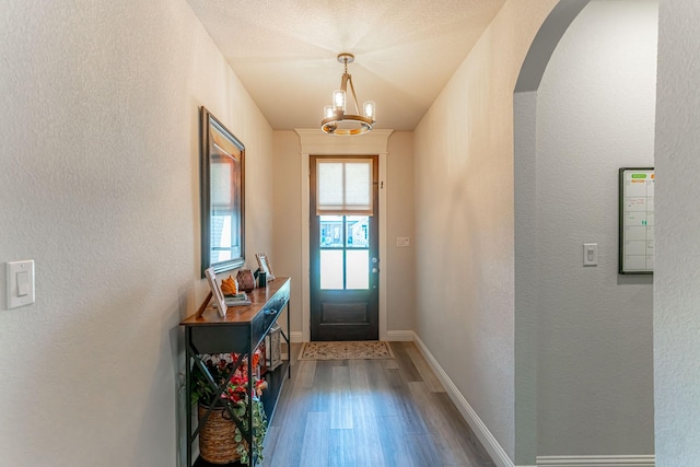doorway featuring arched walkways, dark wood finished floors, baseboards, a chandelier, and a textured wall
