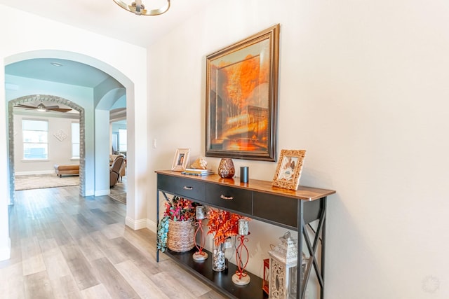 corridor with arched walkways, baseboards, and light wood finished floors