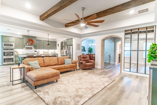 living area with arched walkways, a ceiling fan, visible vents, and light wood-style flooring