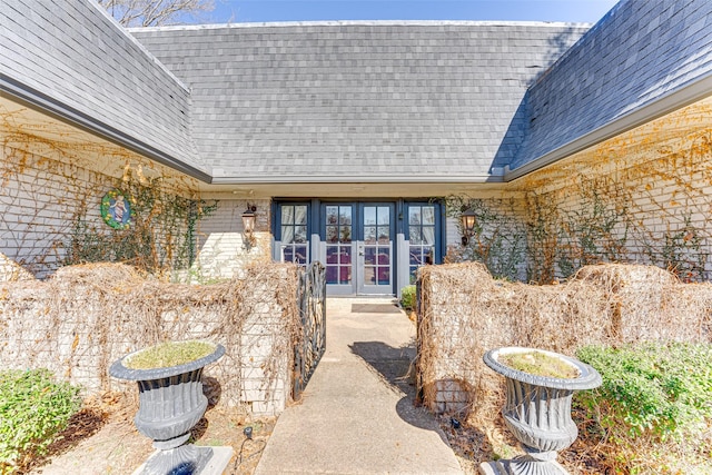view of exterior entry featuring roof with shingles and french doors