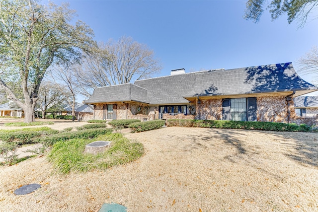 view of front of house featuring a shingled roof, a chimney, mansard roof, and brick siding