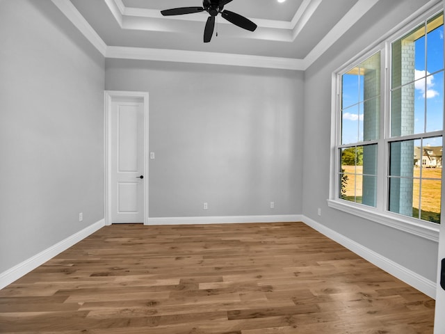 empty room featuring baseboards, ceiling fan, wood finished floors, and a tray ceiling