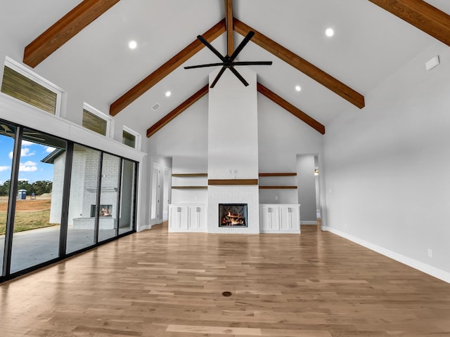 unfurnished living room featuring a large fireplace, beam ceiling, wood finished floors, baseboards, and high vaulted ceiling