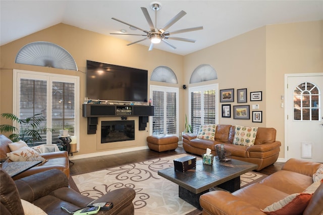 living area featuring ceiling fan, wood finished floors, baseboards, lofted ceiling, and a glass covered fireplace